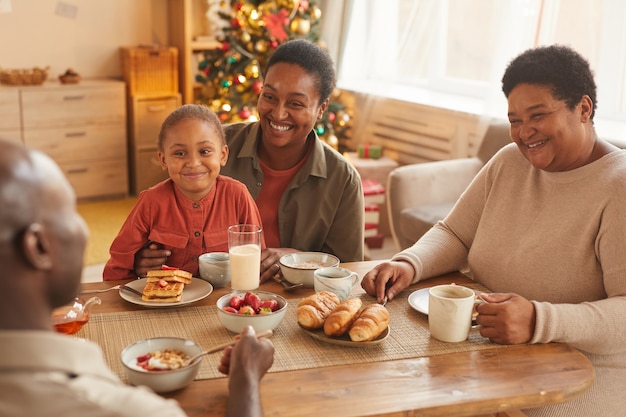 Portrait aux tons chaleureux de l'heureuse famille afro-américaine en dégustant du thé et des collations tout en célébrant Noël à la maison