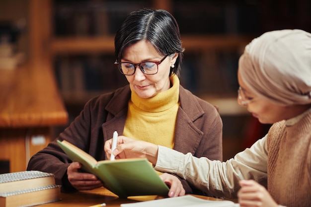 Portrait aux tons chauds de deux étudiantes adultes lisant des livres tout en se préparant à l'examen dans la bibliothèque du collège