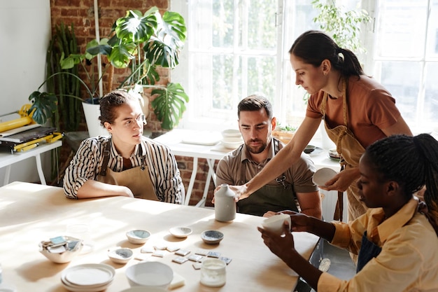 Portrait aux tons chauds d'un groupe diversifié de personnes bénéficiant d'un cours de poterie dans un studio confortable