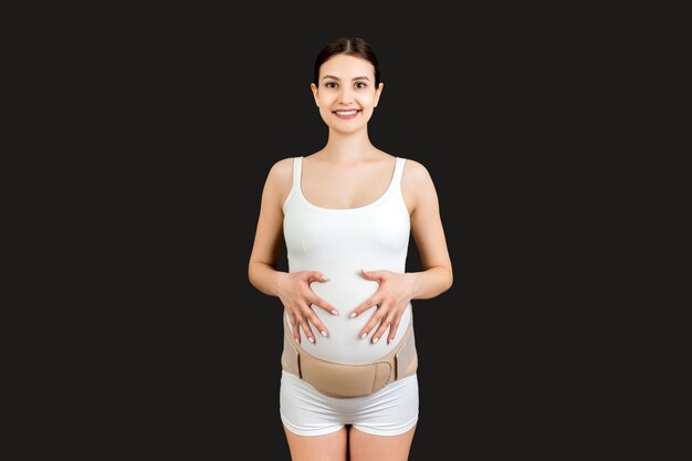 Portrait d'une bande de maternité élastique habillée sur une femme enceinte pour réduire les maux de dos sur fond noir avec espace de copie. Concept de ceinture de soutien abdominale orthopédique.