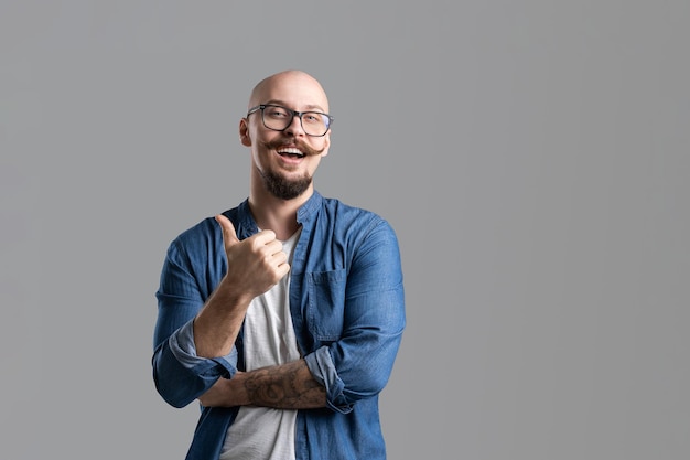 Portrait d'un barbu chauve souriant avec un homme moustache dans des verres montrant le pouce vers le haut sur fond gris