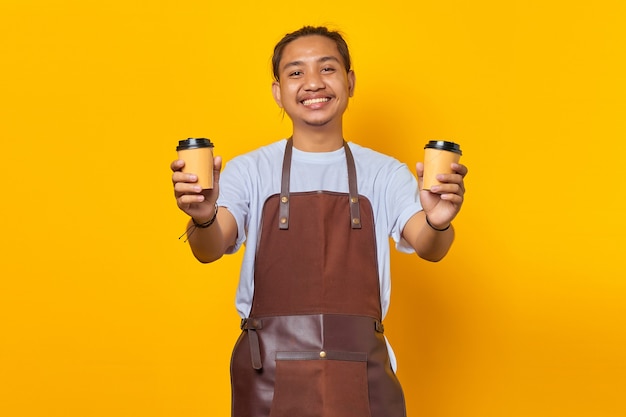 Portrait d'un barista joyeux tenant deux tasses à café en papier à choisir isolé sur fond jaune