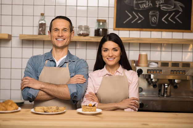 Portrait d'un barista souriant et d'un propriétaire de café avec les bras croisés dans un café en regardant la caméra