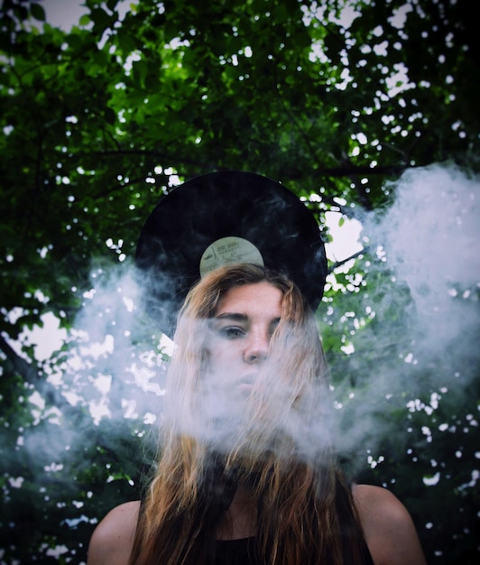 Photo portrait en bas angle d'une femme fumant contre des arbres