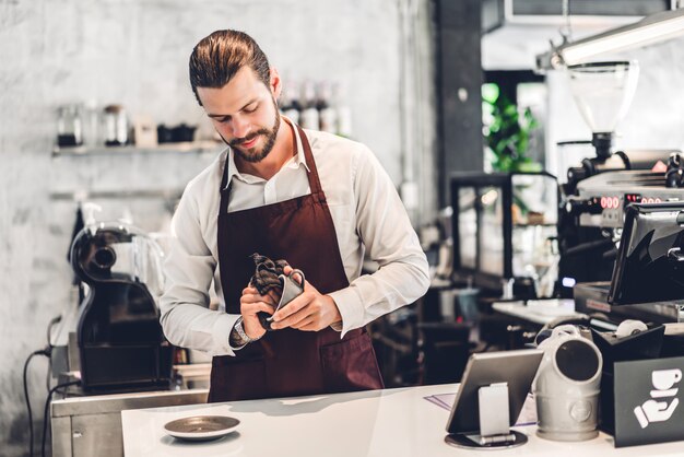 Portrait de beau barista barbu homme propriétaire de petite entreprise souriant et tenant une tasse de café dans le café ou le café.Barista mâle debout au café