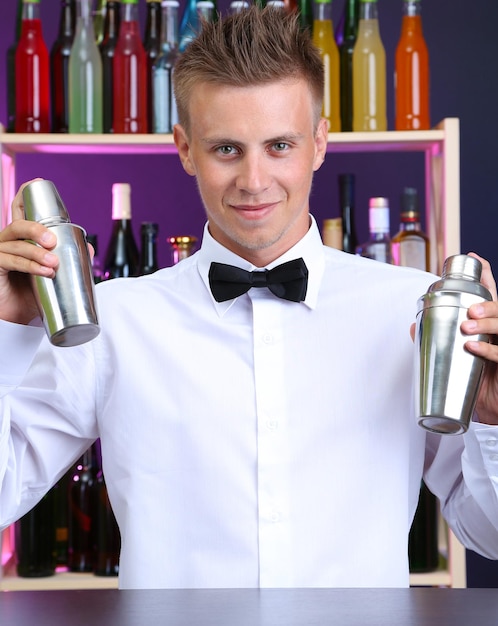 Photo portrait de beau barman avec deux shakers au bar