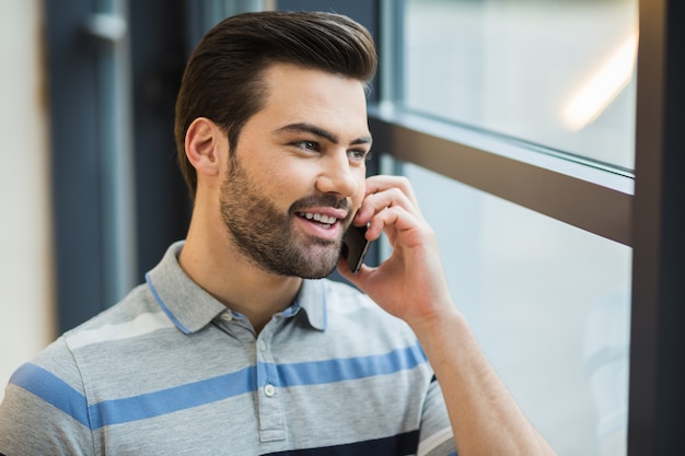 Portrait d'un beau bel homme positif souriant tout en parlant au téléphone