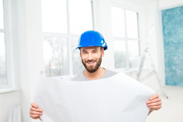 Portrait d'un beau constructeur, contremaître ou réparateur dans le casque avec des dessins sur papier à l'intérieur blanc