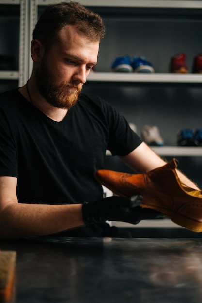 Portrait d'un beau cordonnier barbu examinant des chaussures en cuir marron clair pendant les travaux de restauration. Concept de travaux de réparation et de restauration d'artisan cordonnier dans un atelier de réparation de chaussures.