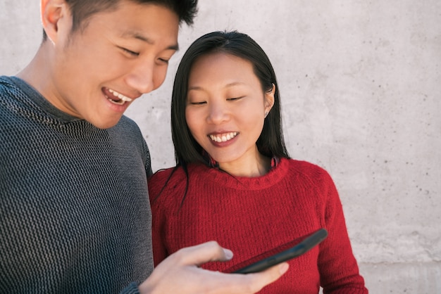 Portrait de beau couple asiatique regardant le téléphone mobile tout en passant du bon temps ensemble. Concept d'amour et de technologie.