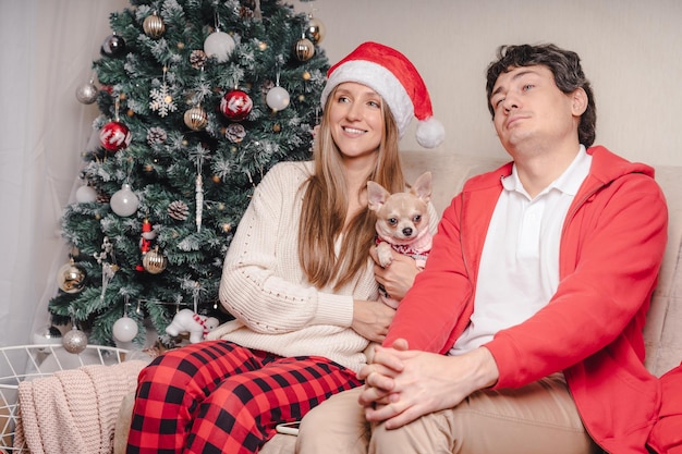 Portrait d'un beau couple mari et femme en bonnet de noel rouge regardant la télévision profiter du temps de Noël à la maison