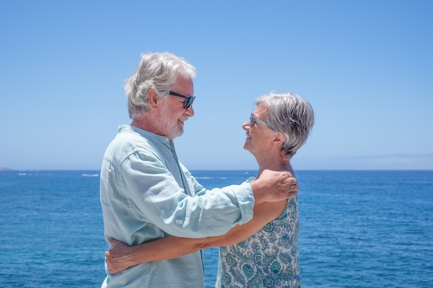 Portrait d'un beau couple de personnes âgées debout au bord de la mer, profitant de l'été et du soleil