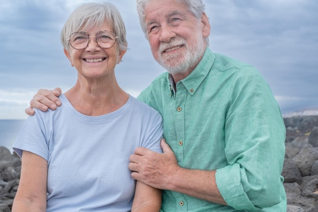 Portrait d'un beau couple de personnes âgées souriant assis et étreignant sur la falaise regardant loin Ciel nuageux dans l'espace de copie d'arrière-plan