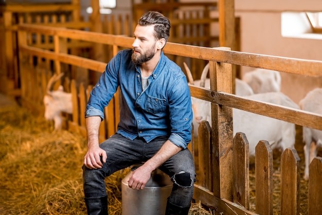 Portrait d'un beau fermier assis sur le récipient à lait rétro à la grange à chèvres. Production de lait naturel et concept d'élevage