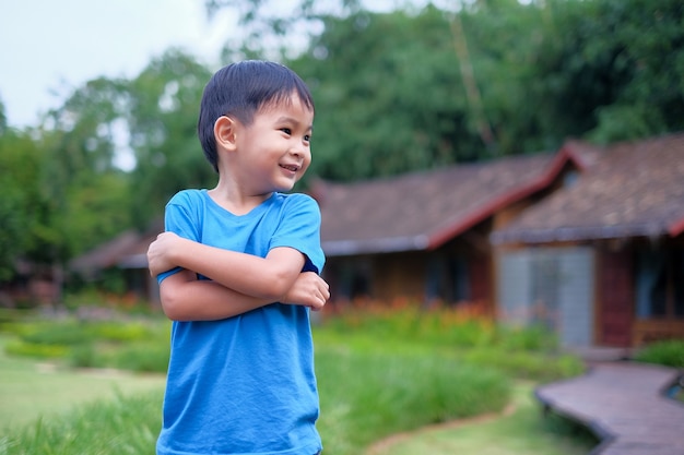 Portrait d&#39;un beau garçon asiatique dans le parc, debout avec les bras croisés et souriant