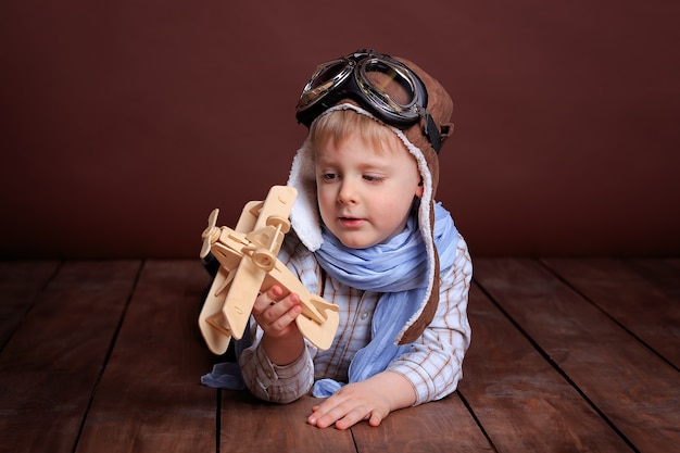 Portrait d'un beau garçon dans un casque de pilote et un foulard bleu avec un avion en bois