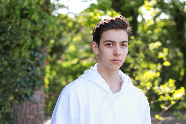 Photo portrait de beau garçon sérieux adolescent en sweat à capuche blanc dans le parc en plein air à la belle journée ensoleillée.