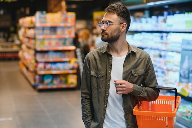 Portrait d'un beau homme souriant faisant ses courses au supermarché en choisissant des produits alimentaires sur l'étagère