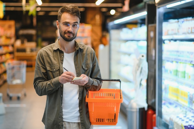 Portrait d'un beau homme souriant faisant ses courses au supermarché en choisissant des produits alimentaires sur l'étagère