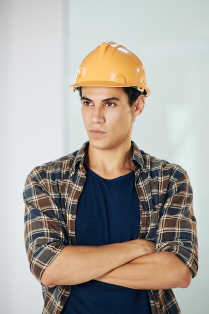 Portrait de beau jeune constructeur jeune métisse sérieux dans les bras croisés casque et à l'écart