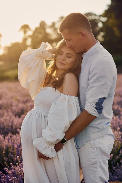 Portrait d'un beau jeune couple enceinte sur un champ de lavande au coucher du soleil Concept de famille heureuse