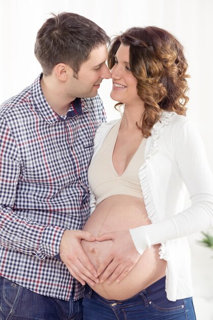 Portrait d'un beau jeune couple faisant une forme de coeur sur le ventre enceinte de la femme.