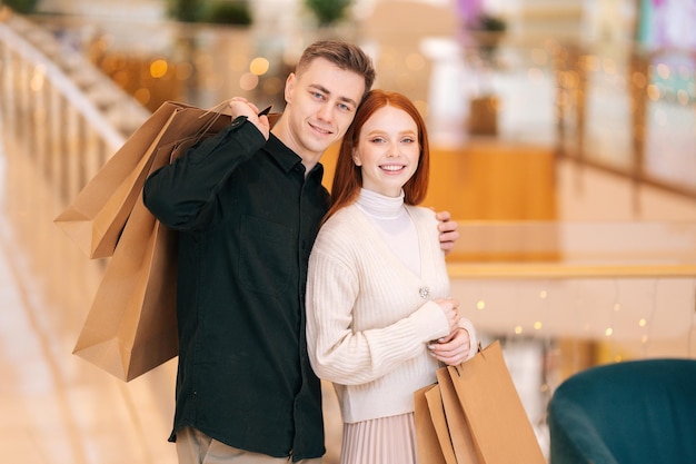 Portrait d'un beau jeune couple heureux tenant des sacs en papier avec des achats et regardant