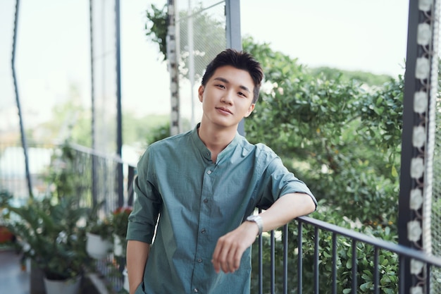 Un portrait d'un beau jeune homme adulte qui s'appuie sur une balustrade, avec le soleil qui brille et les arbres autour.