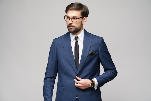 Portrait d'un beau jeune homme d'affaires élégant portant des lunettes sur le mur gris