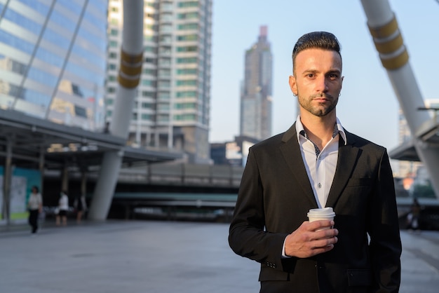 Portrait de beau jeune homme d'affaires italien à l'extérieur en ville portant costume