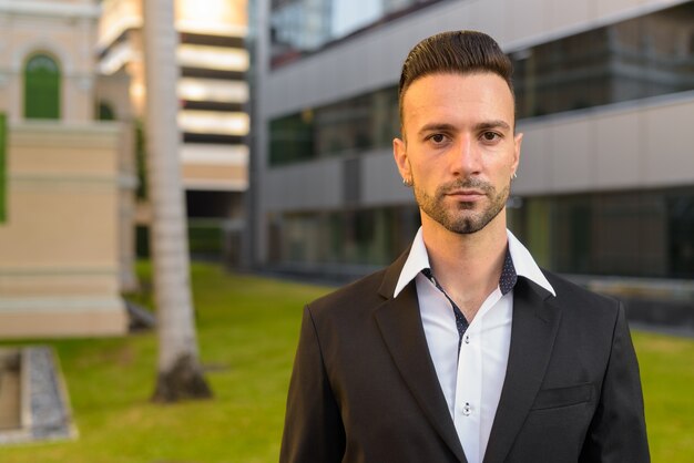 Portrait de beau jeune homme d'affaires italien à l'extérieur en ville portant costume