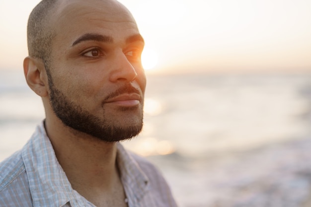 Portrait d'un beau jeune homme américain pendant le coucher du soleil à la plage, gros plan