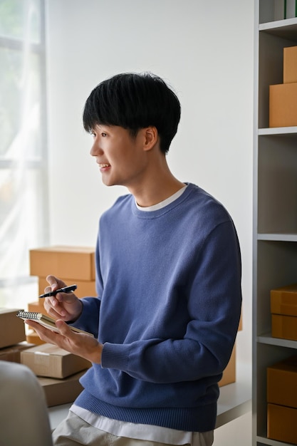 Le portrait d'un beau jeune homme asiatique propriétaire d'une boutique en ligne est assis sur une table