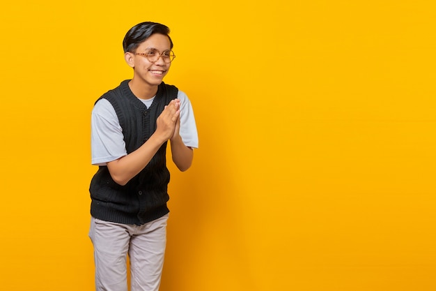 Portrait d'un beau jeune homme asiatique saluant avec un grand sourire sur son visage sur fond jaune