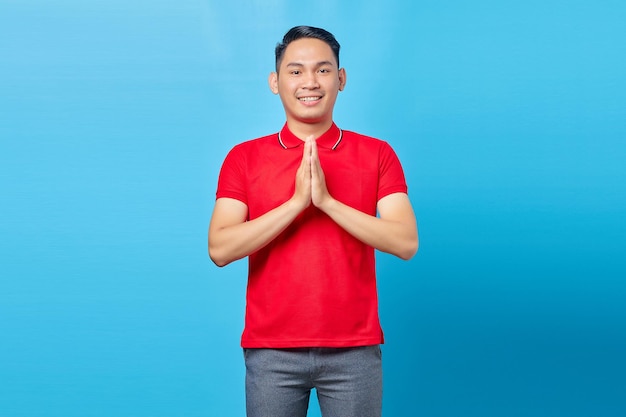 Portrait d'un beau jeune homme asiatique souriant et montrant un geste de salutation vers isolé sur fond bleu