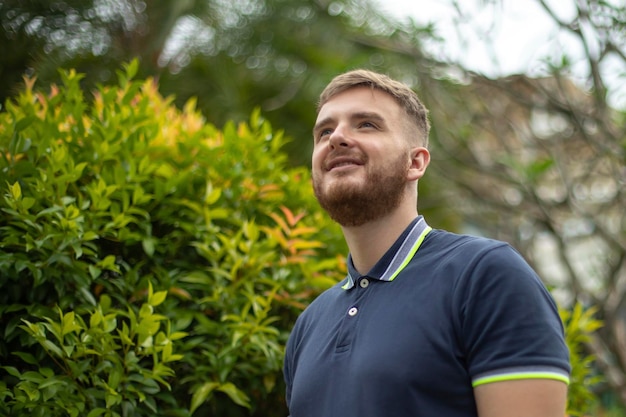 Portrait d'un beau jeune homme barbu avec une barbe debout sur un mur de lierre ou dans la verdure souriant contre un type de plante relaxant à l'extérieur le jour d'été ensoleillé Amour nature eco life