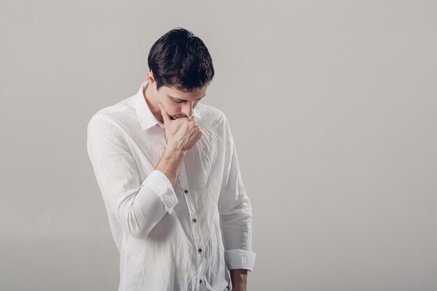 Portrait de beau jeune homme brune songeur en chemise blanche sur fond gris. Lumière douce