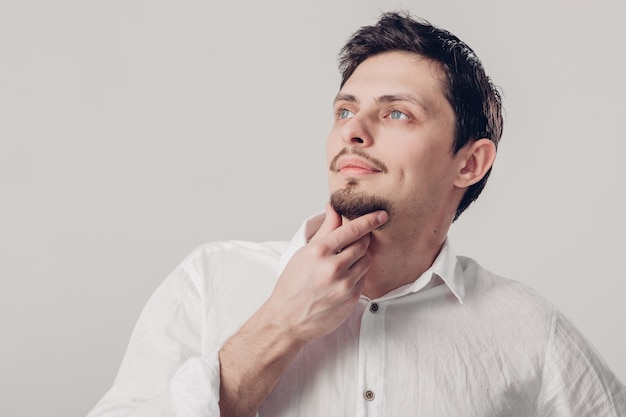 Portrait de beau jeune homme brune songeur en chemise blanche sur fond gris. Lumière douce