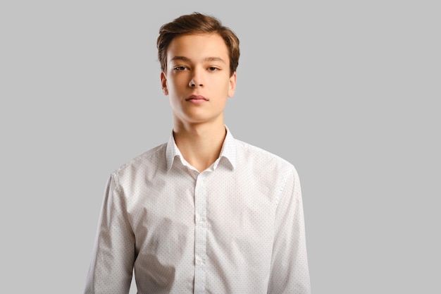 Portrait de beau jeune homme en chemise blanche sur fond de studio gris