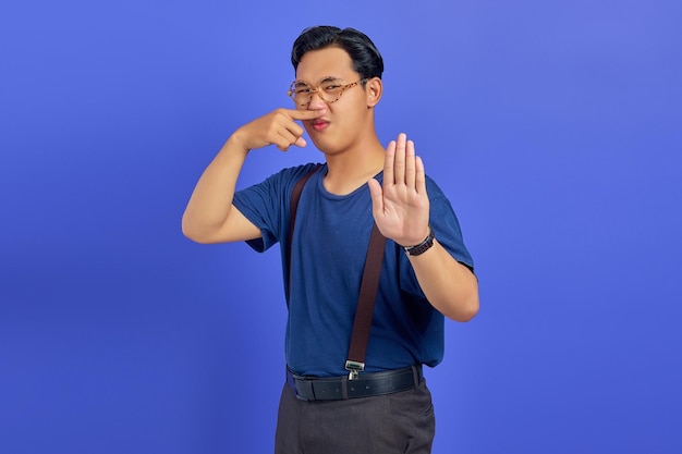 Portrait d'un beau jeune homme en colère faisant un geste d'arrêt avec les paumes et couvrant le nez avec les mains sur fond violet