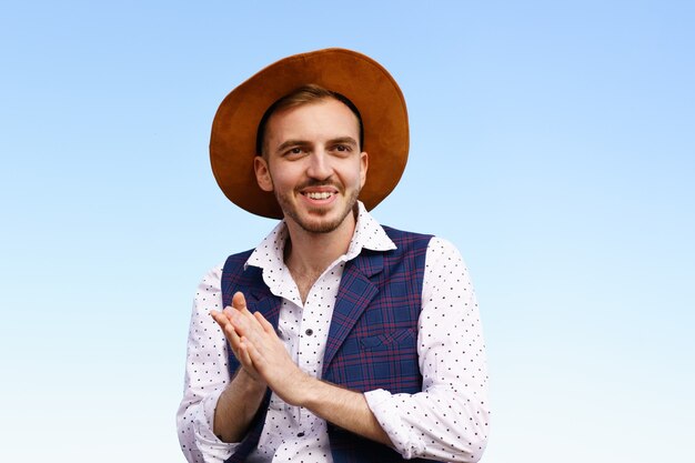 Portrait d'un beau jeune homme dans un chapeau contre un type caucasien de ciel bleu avec une barbiche souriant hap...