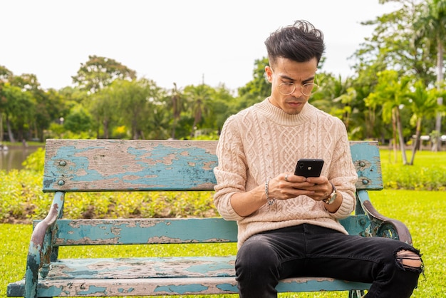 Portrait de beau jeune homme dans le parc pendant l'été à l'aide de téléphone