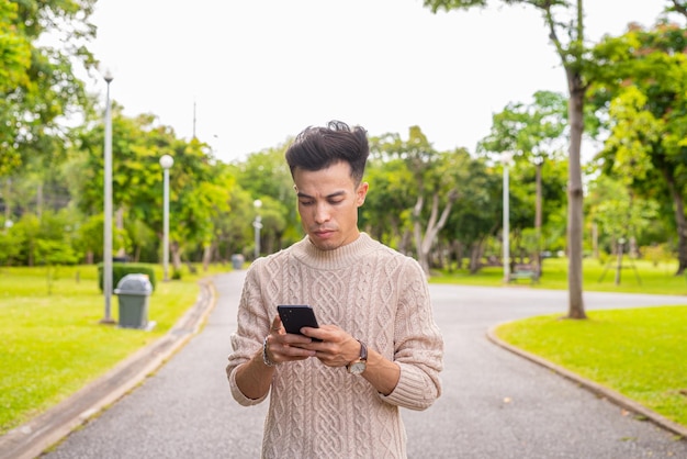 Portrait de beau jeune homme dans le parc pendant l'été à l'aide de téléphone