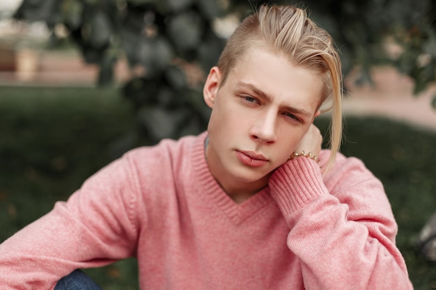 Portrait d'un beau jeune homme dans un pull rose dans le parc