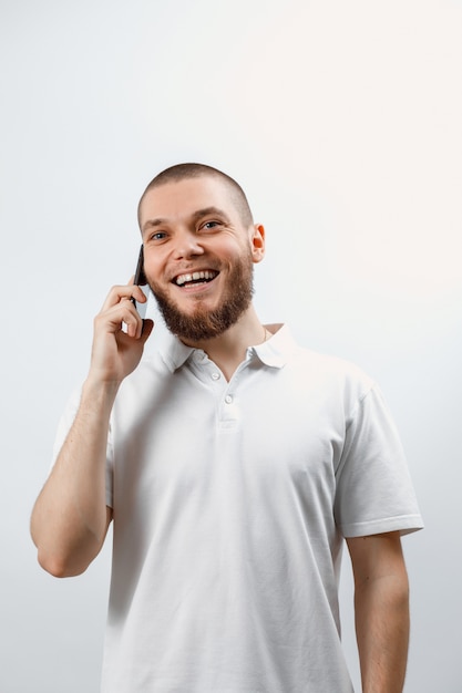 Portrait d'un beau jeune homme dans un T-shirt blanc parlant sur smartphone sur blanc