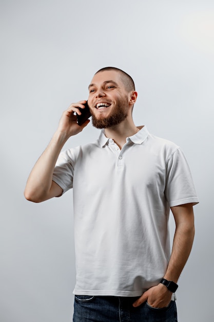 Portrait d'un beau jeune homme dans un T-shirt blanc parlant sur smartphone sur blanc