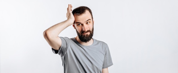 Portrait d'un beau jeune homme fronçant les sourcils tout en se tenant la main près de la tête sur fond blanc avec un espace pour la maquette publicitaire