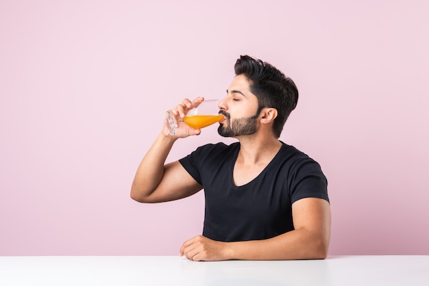 Portrait d'un beau jeune homme indien buvant du jus d'orange dans la cuisine le matin