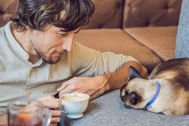 Portrait de beau jeune homme jouant avec un chat et boit du café