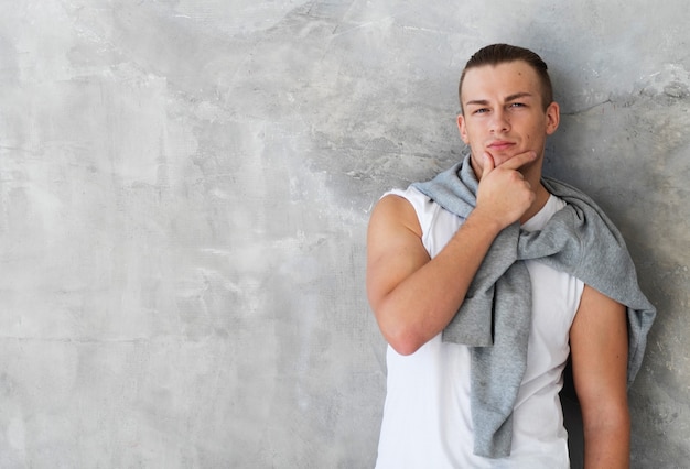 Portrait d'un beau jeune homme, mannequin. Posant sur un mur gris.